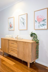 The selection of Australian native floral prints of a Red Waratah, Light Eucalyptus Gum Leaves and Peach Protea native flower in Oak frames by 41 Orchard, sit symmetrically above a blackbutt sideboard with accessories against Lamb's Wool Wattyl low sheen wall making the perfect Australiana look.